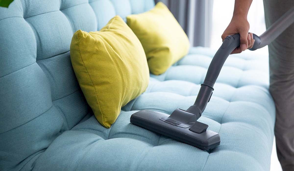 a couch with throw pillows being vacuumed after being steam cleaned